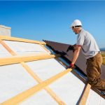 Metal Roof being installed by worker with power tool and white hard hat on