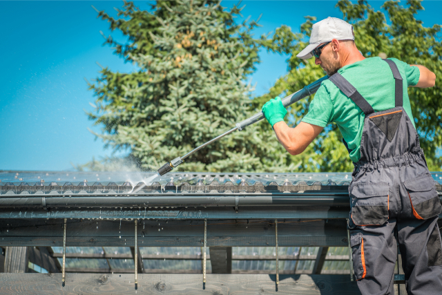 Roof and Gutter Cleaning by worker with a pressure washer