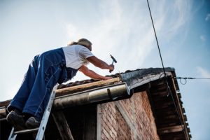 Roof repair by worker on a ladder with a hammer and nails.