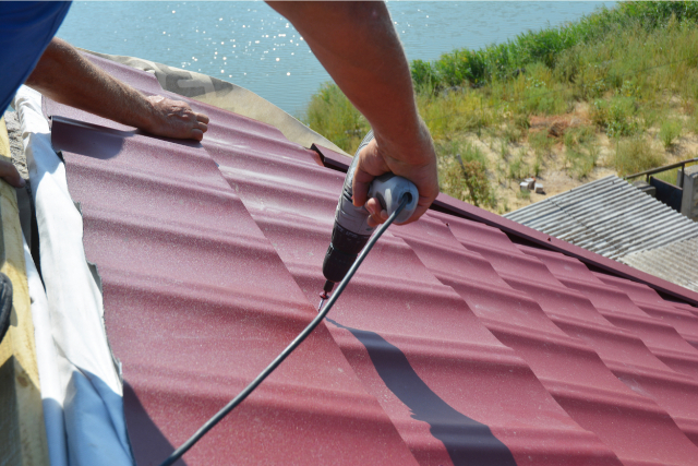 Roofer contractor installing metal roof tile with screwdriver